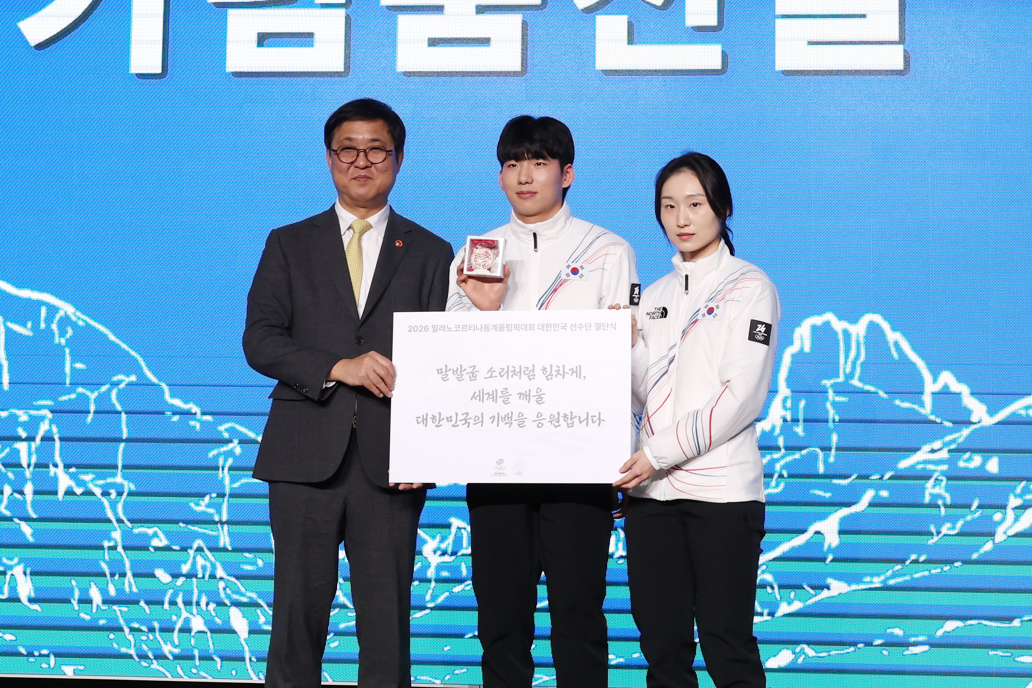 1月22日，在首尔松坡区奥林匹克公园酒店举行的2026年米兰-科尔蒂纳冬奥会韩国体育代表团成团仪式上，文化体育观光部长官崔辉英（左）向运动员郑在原（中）和崔敏静赠予鼓励书信和纪念品。韩宣网记者李廷佑 摄