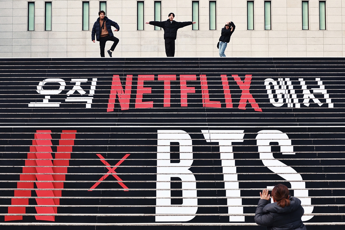 3月17日，首尔市方面表示，为确保21日在光化门广场举行的防弹少年团（BTS）回归演出安全，将为来自世界各地的访客实时提供综合服务信息，确保所有人都能安全、便利地观看演出。图为11日，在首尔钟路区世宗文化会馆前，三位外国游客在宣传防弹少年团（BTS）回归的装饰阶梯上合影留念。图片来源：韩联社