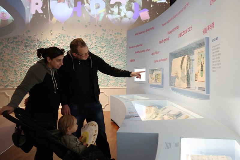 4月7日，在首尔钟路区国立民俗博物馆举行的《生日快乐》特别展中，一家外国游客正在参观韩国传统婴儿背带的演变史。过去在韩国，人们会用一种带有长系带的大块绗缝布作为包被，将婴儿背在背上。这与西方将婴儿抱在怀里的方式不同，韩国的这种传统育儿方式能够增进母婴之间的肌肤接触，从而加强情感联结。韩宣网记者朴大珍 摄 