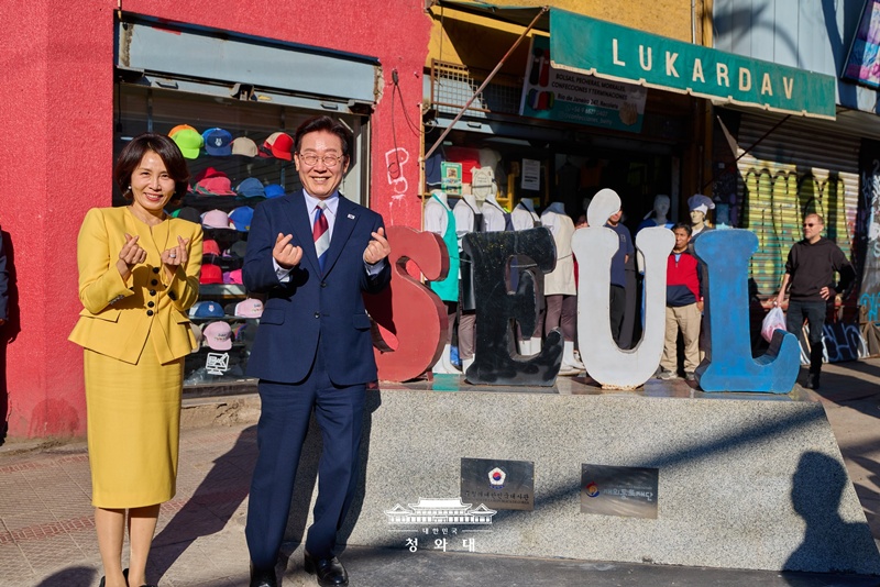 当地时间7月30日，韩国总统李在明与夫人金惠景在智利圣地亚哥雷科莱塔区帕特罗纳托“首尔街”雕塑前，向当地侨胞和居民比出“手指爱心”手势。李在明夫妇当天走访当地韩侨商业区，慰问商户，并与当地侨胞深入交流。图片来源：大韩民国青瓦台