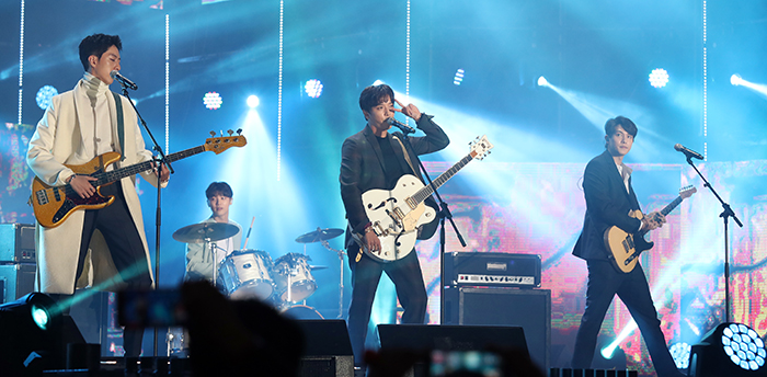 그룹 씨엔블루가 무대에 오른 가운데 정용화가 팬들을 향해 브이를 그려보이며 윙크하고 있다.