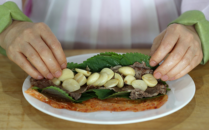 잘 익은 김치를 넓게 펴고 깻잎과 구운 쇠고기, 구운 마늘을 차례로 올려 둥글게 말아낸다.