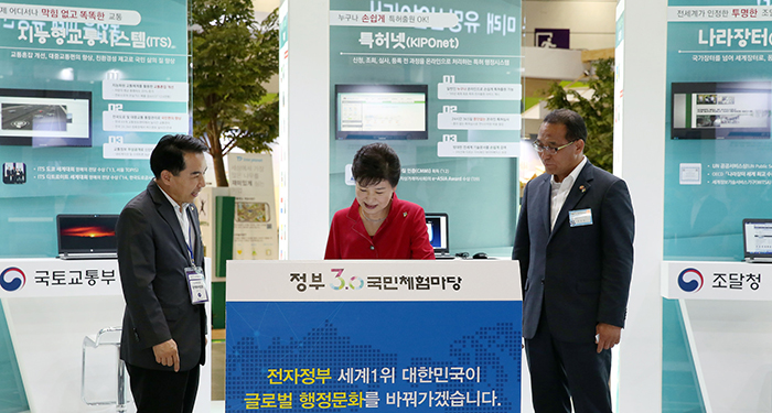 朴总统（中）在政府3.0国民体验场上在听取行政自治部电子政府局长（左）关于电子政府出口的介绍。右边是行政自治部部长洪允植。