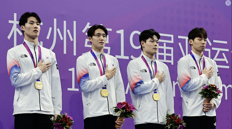 图为9月25日，在杭州奥体中心体育场进行的杭州第19届亚运会男子4×200米自由泳接力赛上，韩国队选手们获得奖牌以后，向国旗敬礼。从左以此为，黄宣优、金禹旻、李昊峻、梁才勋。图片来源：国际奥委会官网