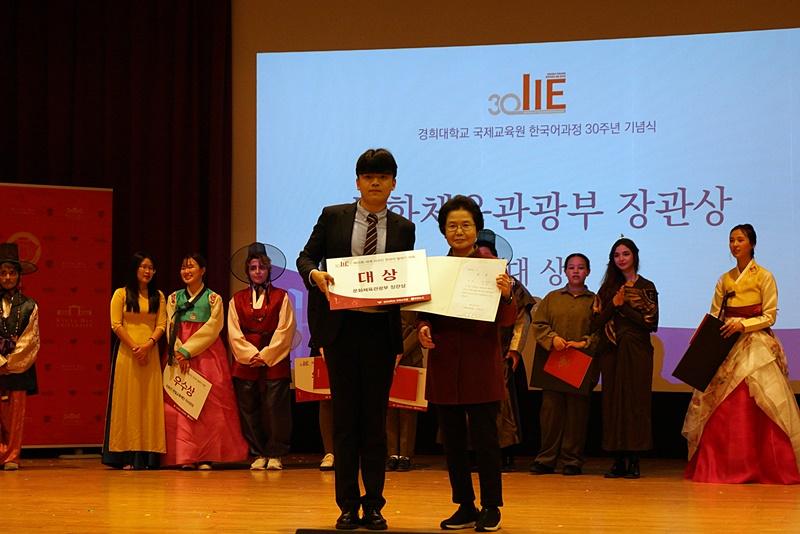 10月19日下午，在首尔东大门区庆熙大学皇冠馆举行的第25届世界外国人韩语演讲大赛上，评审委员安英淑（音，左）为此次大赛最高奖项获奖者谭瑞升颁奖并合影留念。图片来源：庆熙大学国际教育院