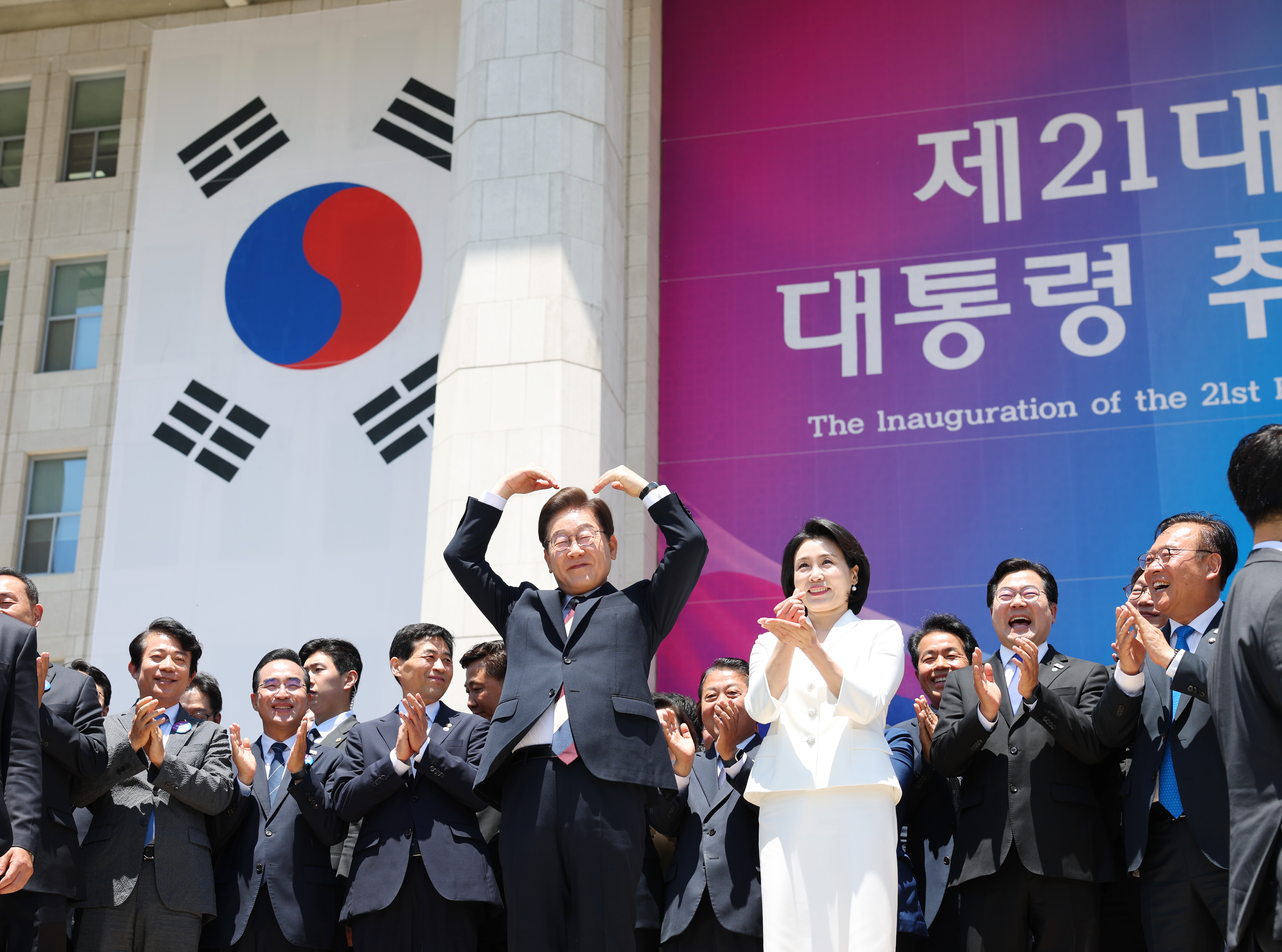 6月4日，在结束第21届总统就职仪式后，韩国总统李在明和夫人金惠景走出场外向支持者们比心致意。随后，在国会舍廊斋，李在明与与国会议长禹元植、朝野各党代表共进午餐。图片来源：政府共同采访团