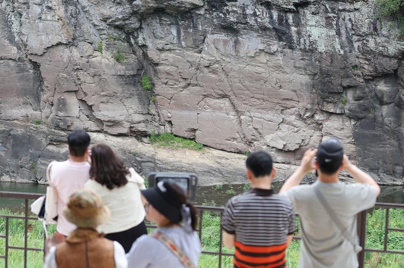 7月13日，在蔚山市蔚州郡大谷里的盘龟台岩刻画瞭望台上，市民们正在用望远镜观察岩刻画。7月12日，由“蔚州大谷里盘龟台岩刻画”和“蔚州川前里铭文和岩刻画”组成的“盘龟川岩刻画”被列入联合国教科文组织世界遗产名录。图片来源：韩联社