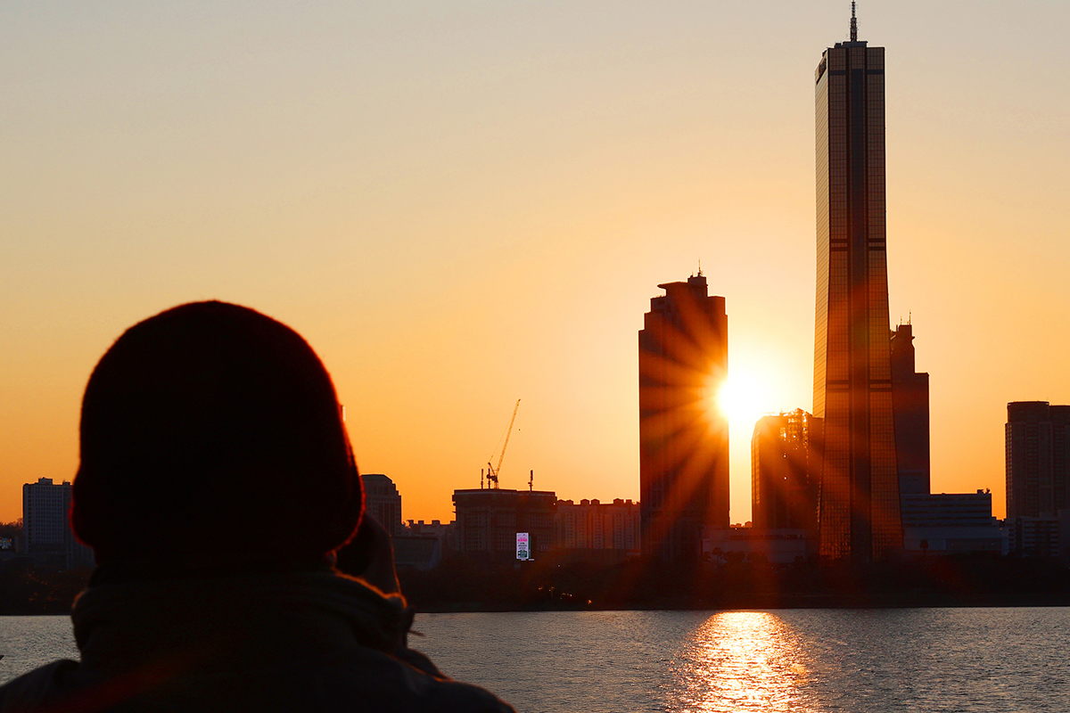 12月30日下午，在首尔龙山区二村汉江公园，一位市民望着被染红的落日，挥别2025年。
