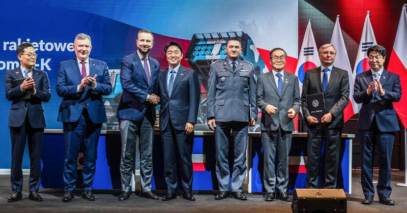 当地时间12月29日，在波兰华沙军事博物馆举行的“天覆第三次执行合同签约仪式”上，韩国总统室秘书室长姜勋植（左四）与波兰副总理兼国防部长瓦迪斯瓦夫·科西尼亚克-卡梅什握手。左起依次为韩华航天代表理事孙在一，波兰国防部副部长帕维乌·贝伊达，（左五起）波兰军备局局长阿图尔·库普特尔，韩国防卫事业厅厅长李熔哲，WB集团董事长皮奥特尔·沃伊切赫，以及韩国国防部资源管理室室长元锺大。图片来源：韩华航天